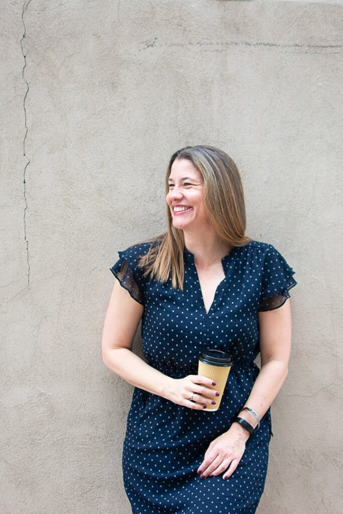 picture of andrea belzer standing against the wall. Holding a cup of coffee.